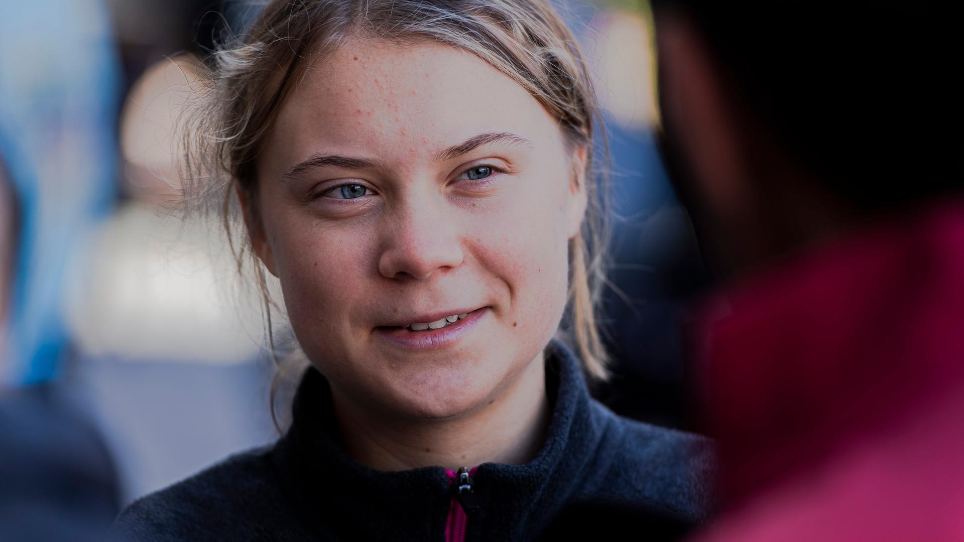 Die schwedische Klimaaktivistin Greta Thunberg schaut freundlich aber ernst eine Person an, mit der sie im Gespräch ist, und die mit dem Rücken zur Kamera steht.