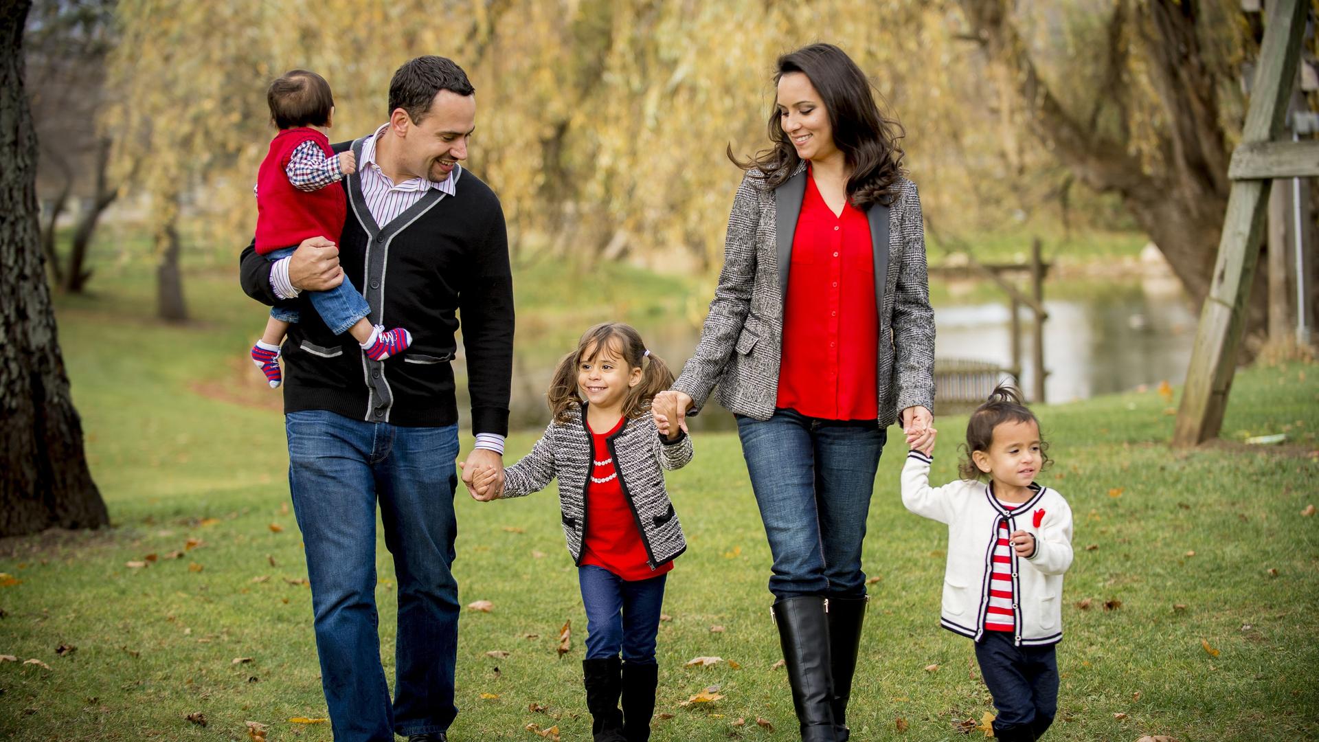 Eine Familie geht in einem Park spazieren, Vater, Mutter und drei Kinder sind lächelnd und händehaltend unterwegs. Eine Familie geht in einem Park spazieren, Vater, Mutter und drei Kinder sind lächelnd und händehaltend unterwegs.