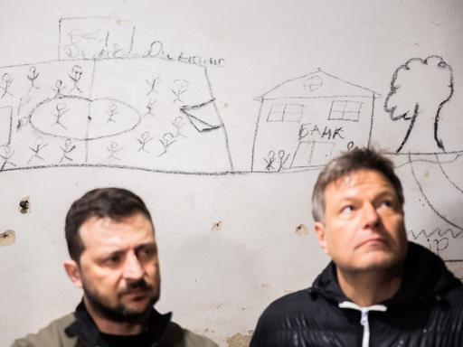 Robert Habeck (Bündnis 90/Die Grünen, r), Bundesminister für Wirtschaft und Klimaschutz, und Wolodymyr Selenskyj, Präsident der Ukraine, stehen nordöstlich von Kiew in einem Schulkeller, in dem Geiseln gehalten wurden vor einer Wand mit Bildern der Gefangenen. 