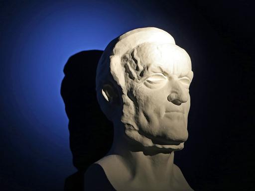 Eine hart angeleuchtete Büste von Richard Wagner vor einem dunkel blauen Hintergrund.