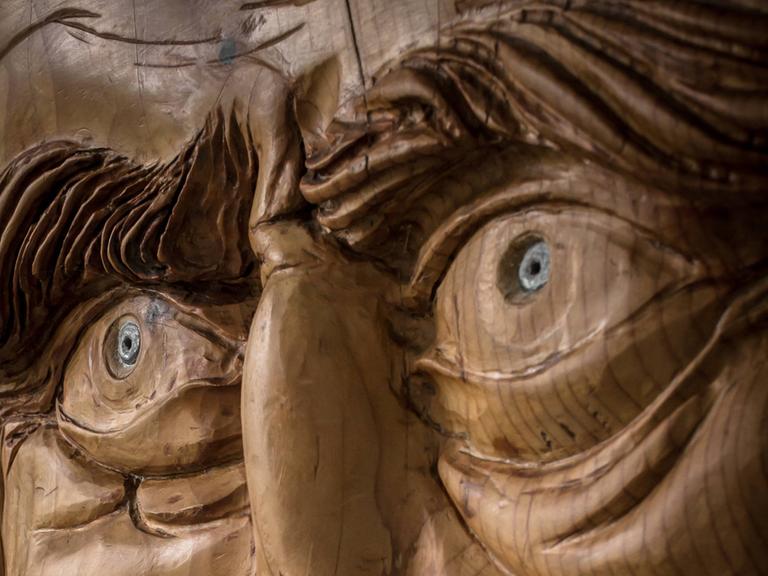 Foto einer Holzarbeit, die das Gesicht mit markanten Augen und Augenbrauen eines alten Mannes zeigt.
