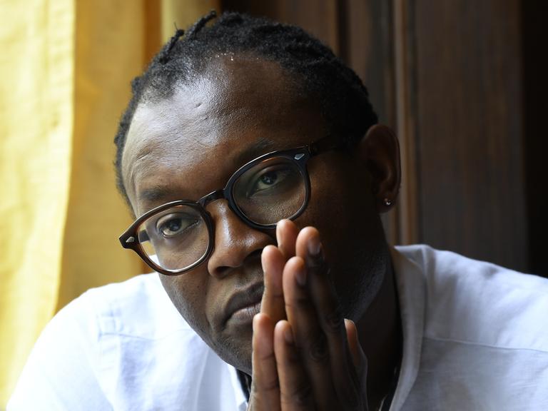 Der kongolesische Autor Fiston Mwanza Mujila während eines Interviews. Er legt die Handflächen vor seinem Gesicht aneinander.