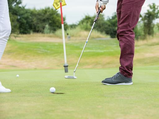 Ein Golfspieler locht auf einem Golfplatz in Köln den Golfball ein.