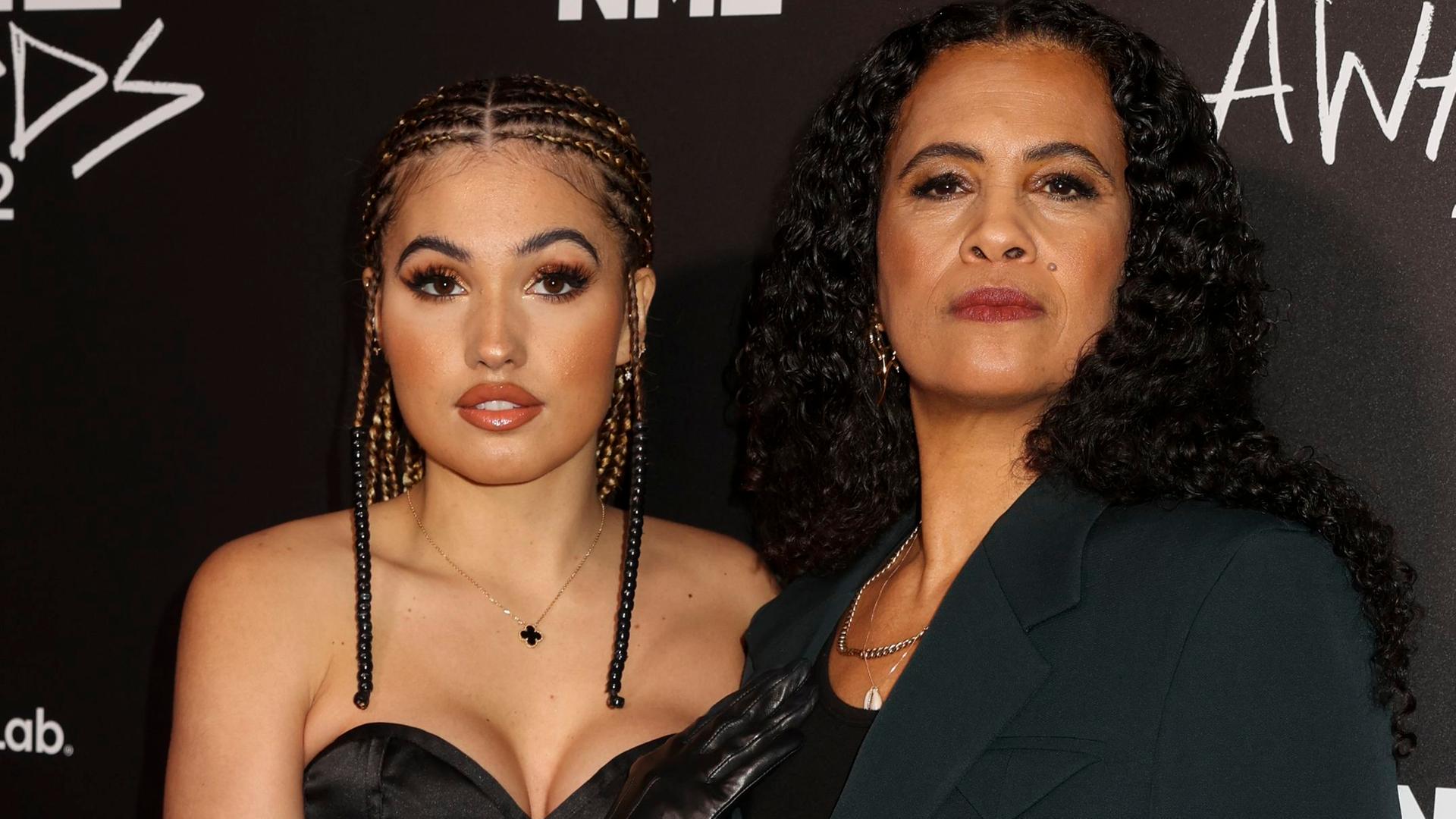 Popstar Mabel und ihre Mutter, Neneh Cherry, stehen vor schwarzem Hintergrund, auf dem oben in weiß die Buchstaben NME stehen. Mabel trägt ein Kleid, ihr Haar hat sie zu vielen kleinen Zöpfen geflochten. 80er-Jahre-Superstar Neneh Cherry trägt ihre langen, schwarzen Haare offen, sie trägt einen Hosenanzug. Beide schauen in die Kamera. Popstar Mabel und ihre Mutter, Neneh Cherry, stehen vor schwarzem Hintergrund, auf dem oben in weiß die Buchstaben NME stehen. Mabel trägt ein Kleid, ihr Haar hat sie zu vielen kleinen Zöpfen geflochten. 80er-Jahre-Superstar Neneh Cherry trägt ihre langen, schwarzen Haare offen, sie trägt einen Hosenanzug. Beide schauen in die Kamera.
