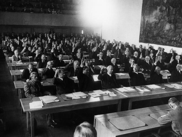 Annahme des Grundgesetzes: Das Plenum des Parlamentarischen Rates nimmt in 3. Lesung am 8. Mai 1949 den revidierten Grundgesetzentwurf mit 53 gegen 12 Stimmen an.