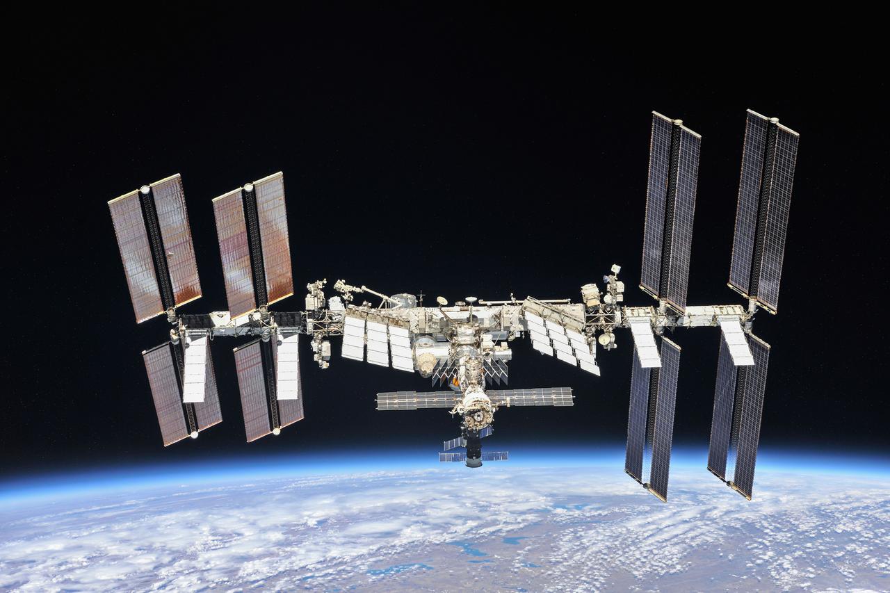 Die Internationale Raumstation in der Schwärzes des Alls, am unteren Bildrand der blaue Planet Erde