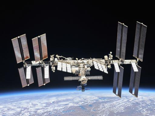Die Internationale Raumstation in der Schwärzes des Alls, am unteren Bildrand der blaue Planet Erde