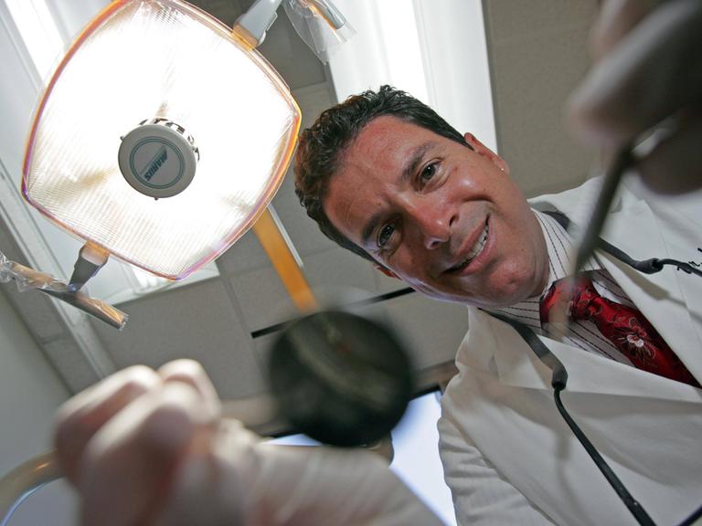 Der Zahnarzt Dr. Jay Grossmann beugt sich über einen Behandlungsstuhl mit seinen Instrumenten zur Zahnbehandlung.