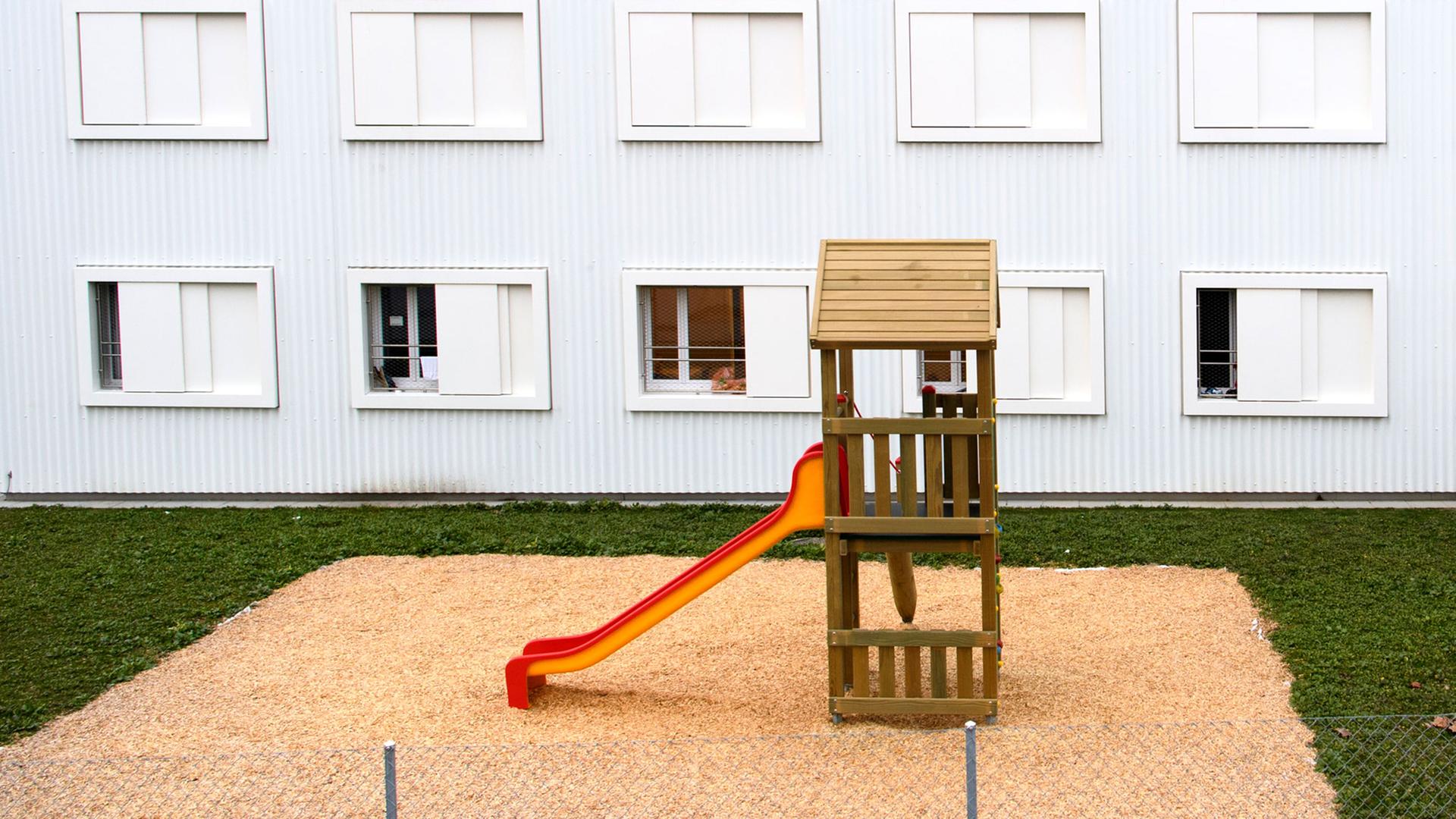 "Welcher Art die Wärme ist" - Hörspiel-Collage über Migrationsgeschichten der Schweiz. Zu sehen: Ein Sandkasten mit einer Rutsche vor einer Geflüchteten-Unterkunft. "Welcher Art die Wärme ist" - Hörspiel-Collage über Migrationsgeschichten der Schweiz. Zu sehen: Ein Sandkasten mit einer Rutsche vor einer Geflüchteten-Unterkunft.