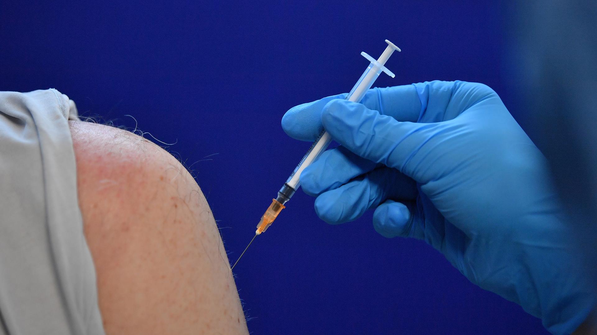 An einem Oberarm wird eine Spritze mit einem Vakzin gegen das Coronavirus angesetzt.