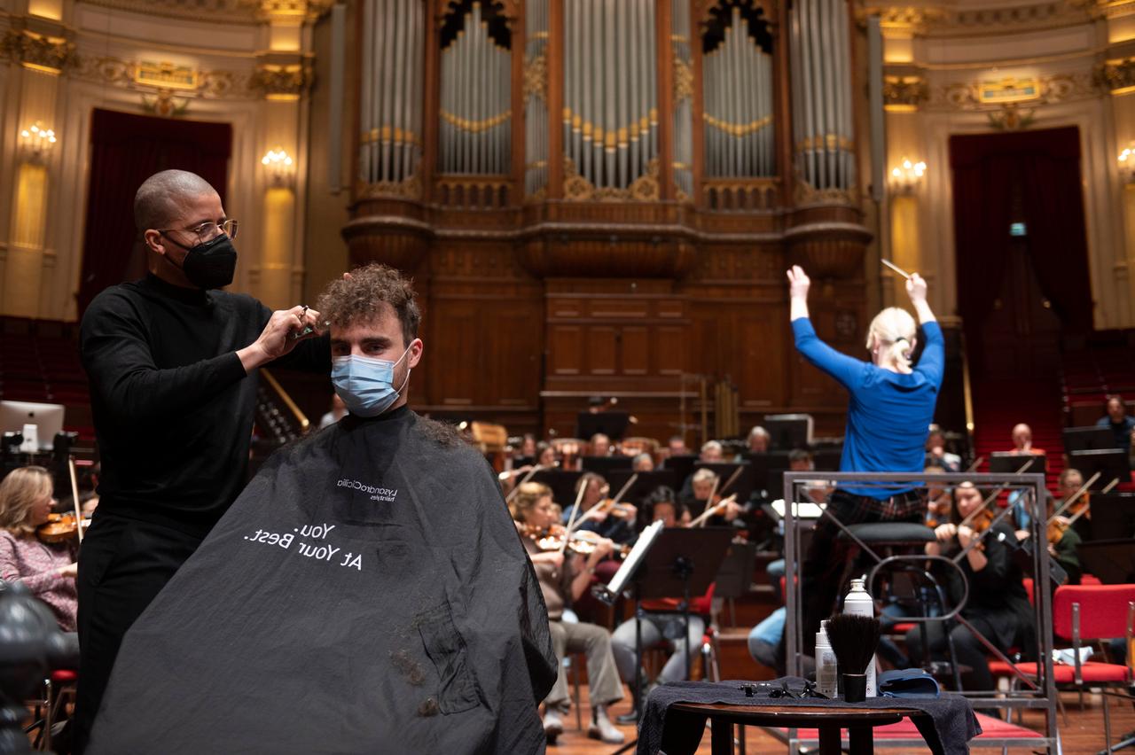 In der Amsterdamer Philharmonie - dem Concertgebouw - lässt sich ein Besucher während eines Konzerts die Haare schneiden. Im Hintergrund sind die Orchestermusiker zu sehen. In der Amsterdamer Philharmonie - dem Concertgebouw - lässt sich ein Besucher während eines Konzerts die Haare schneiden. Im Hintergrund sind die Orchestermusiker zu sehen.