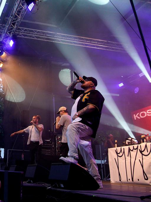 Der Rapper Lugatti steht bei einem Konzert mit einem Mikrofon in der Hand auf der Bühne.
