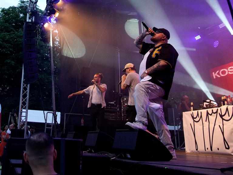 Der Rapper Lugatti steht bei einem Konzert mit einem Mikrofon in der Hand auf der Bühne.