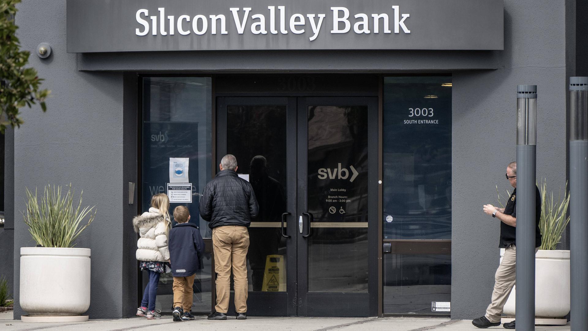 Vor einer Filiale der Silicon Valley Bank lesen ein älterer Mann und zwei Kinder eine an der Tür ausgehängte Bekanntmachung. Vor einer Filiale der Silicon Valley Bank lesen ein älterer Mann und zwei Kinder eine an der Tür ausgehängte Bekanntmachung.