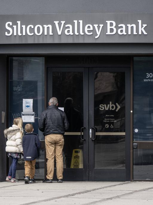 Vor einer Filiale der Silicon Valley Bank lesen ein älterer Mann und zwei Kinder eine an der Tür ausgehängte Bekanntmachung.