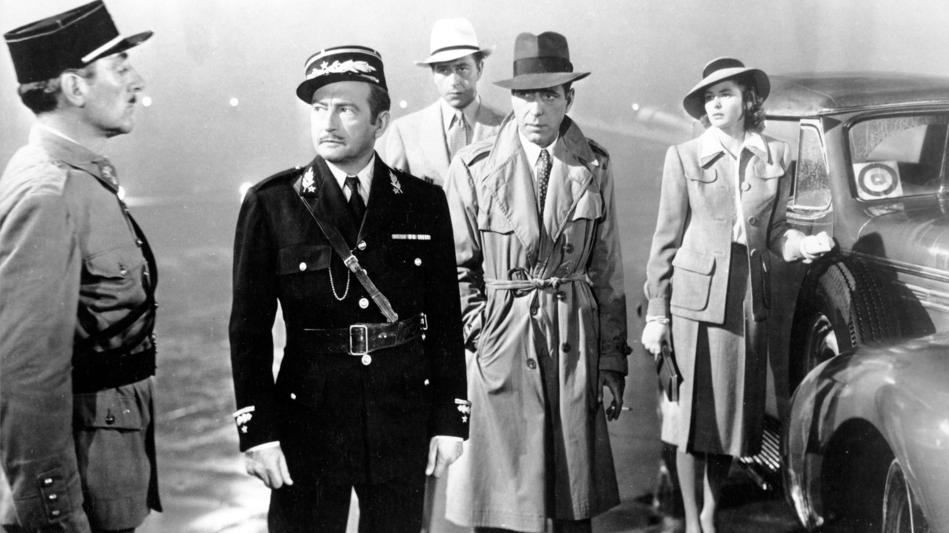 Casablanca. Mehrere Personen stehen bei Regenwetter auf einem Platz. Zwei Personen in Uniform, drei weitere Personen in Zivilkleidung. Casablanca. Mehrere Personen stehen bei Regenwetter auf einem Platz. Zwei Personen in Uniform, drei weitere Personen in Zivilkleidung.