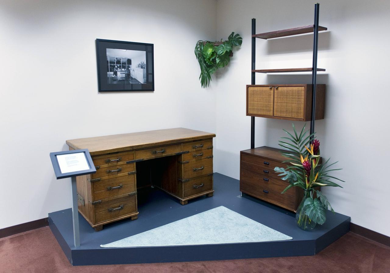 Ein hölzerner Schreibtisch mit Schubladen ist im Museum auf einem Podest ausgestellt. Regale und Zimmerpflanze komplettieren den Ausschnitt einer Büroeinrichtung. Ein hölzerner Schreibtisch mit Schubladen ist im Museum auf einem Podest ausgestellt. Regale und Zimmerpflanze komplettieren den Ausschnitt einer Büroeinrichtung.