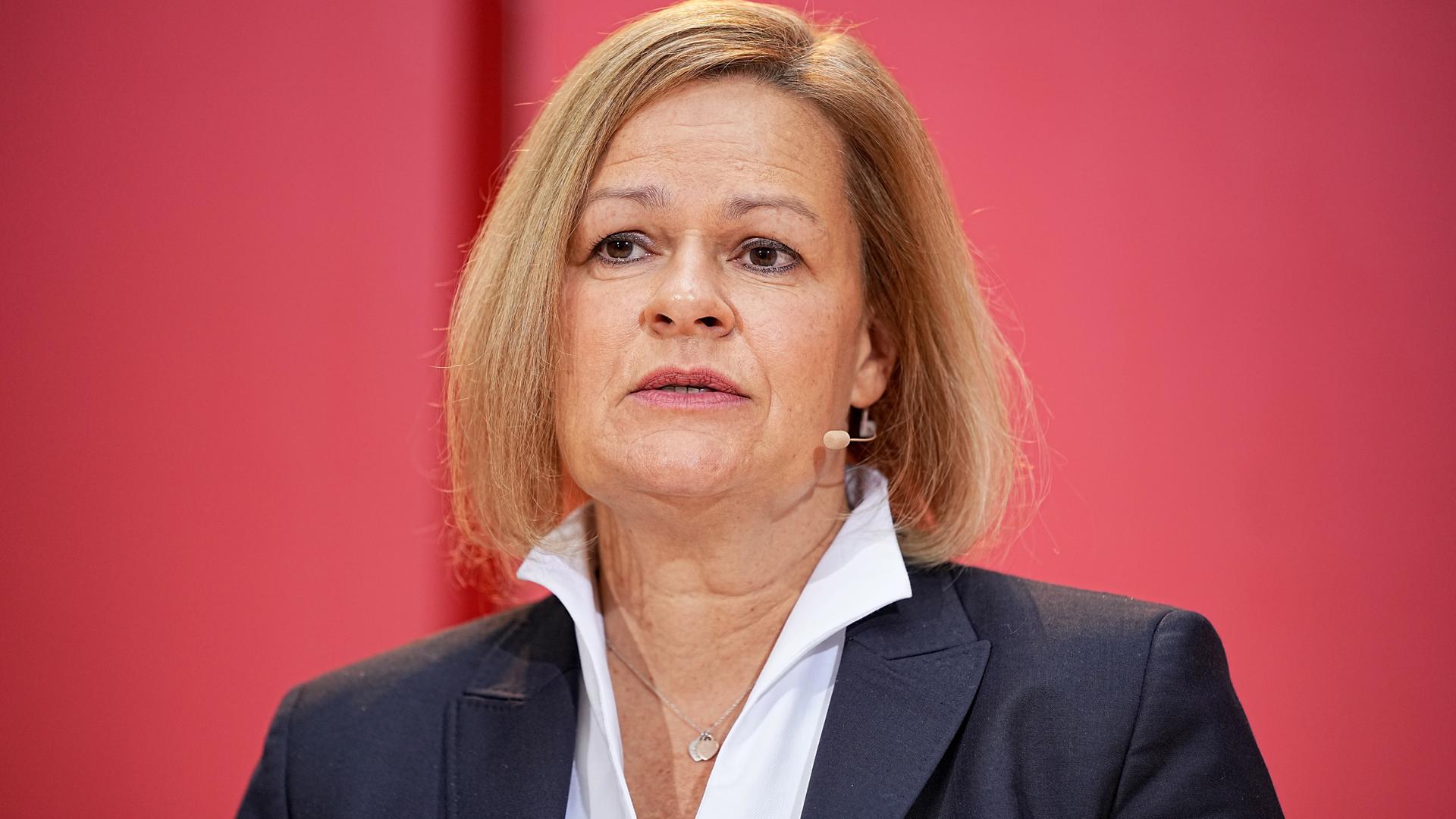 Nancy Faeser mit dunklem Jackett und weißem Hemd vor einer roten Wand. Nancy Faeser mit dunklem Jackett und weißem Hemd vor einer roten Wand.