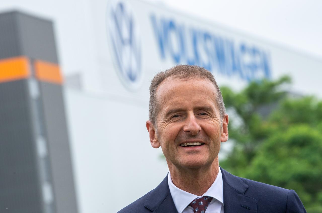 Porträt von Herbert Diess. Im Hintergrund steht an einer Halle der Schriftzug von Volkswagen. Porträt von Herbert Diess. Im Hintergrund steht an einer Halle der Schriftzug von Volkswagen.