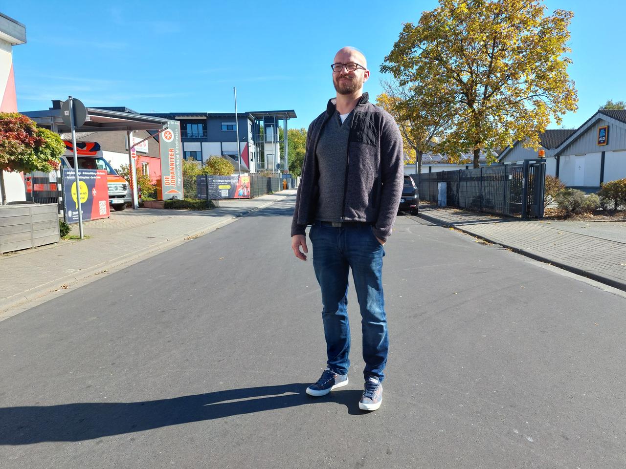 Ein junger Mann steht auf einer Straße, die linke Hand in der Hosentasche. Ein junger Mann steht auf einer Straße, die linke Hand in der Hosentasche.