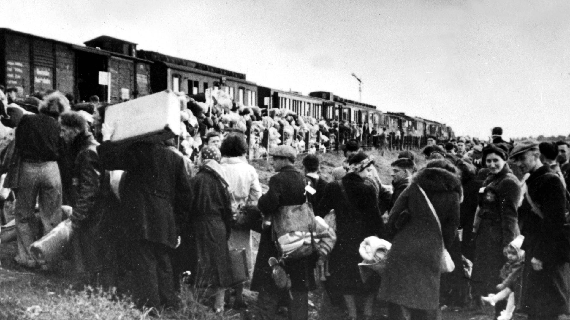 Schwarzweiß Aufnahme von Menschen mit Gepäck, die in einen Güterzug einsteigen Schwarzweiß Aufnahme von Menschen mit Gepäck, die in einen Güterzug einsteigen