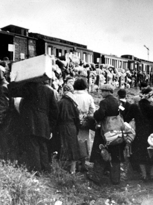 Schwarzweiß Aufnahme von Menschen mit Gepäck, die in einen Güterzug einsteigen