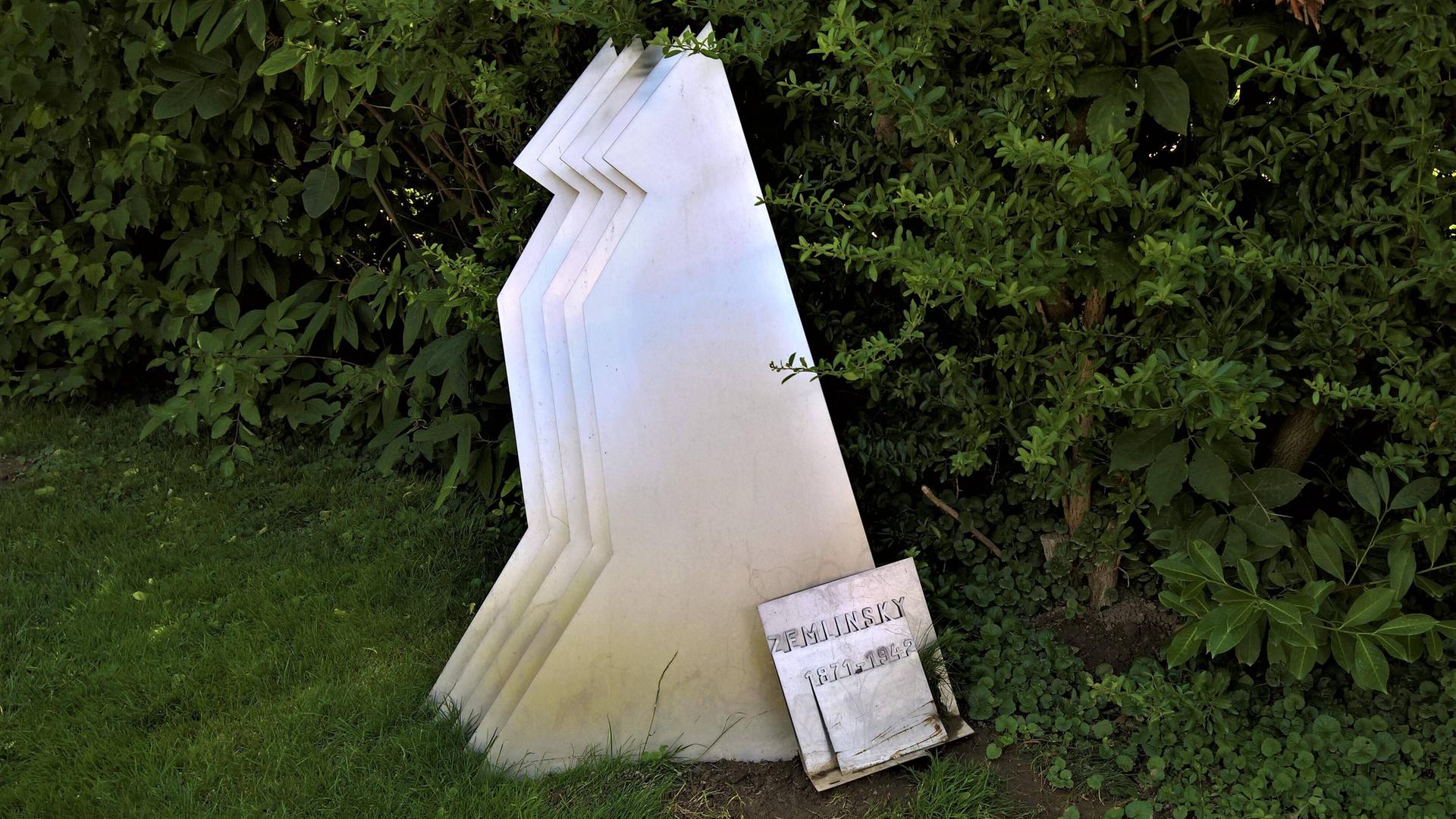 Auf einer Wiese zeigt sich die Grabstele von Alexander von Zemlinsky, die stilisiert wie ein wartender Hund aussieht. Auf einer Wiese zeigt sich die Grabstele von Alexander von Zemlinsky, die stilisiert wie ein wartender Hund aussieht.