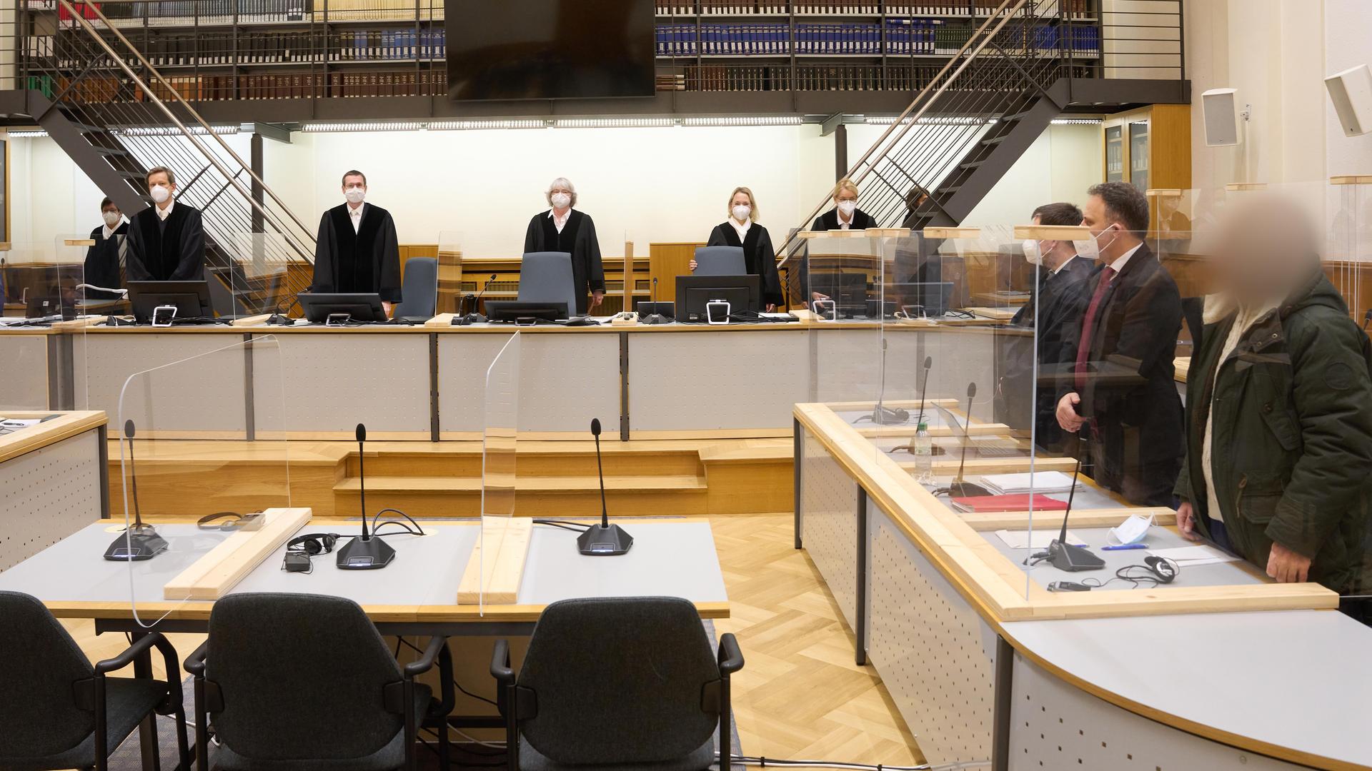 Prozess um Staatsfolter in Syrien. Der Angeklagte (r) und die anderen Prozessbeteiligten stehen im Gerichtssaal des Oberlandesgerichts. Prozess um Staatsfolter in Syrien. Der Angeklagte (r) und die anderen Prozessbeteiligten stehen im Gerichtssaal des Oberlandesgerichts.