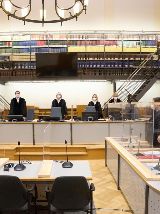 Prozess um Staatsfolter in Syrien. Der Angeklagte (r) und die anderen Prozessbeteiligten stehen im Gerichtssaal des Oberlandesgerichts.