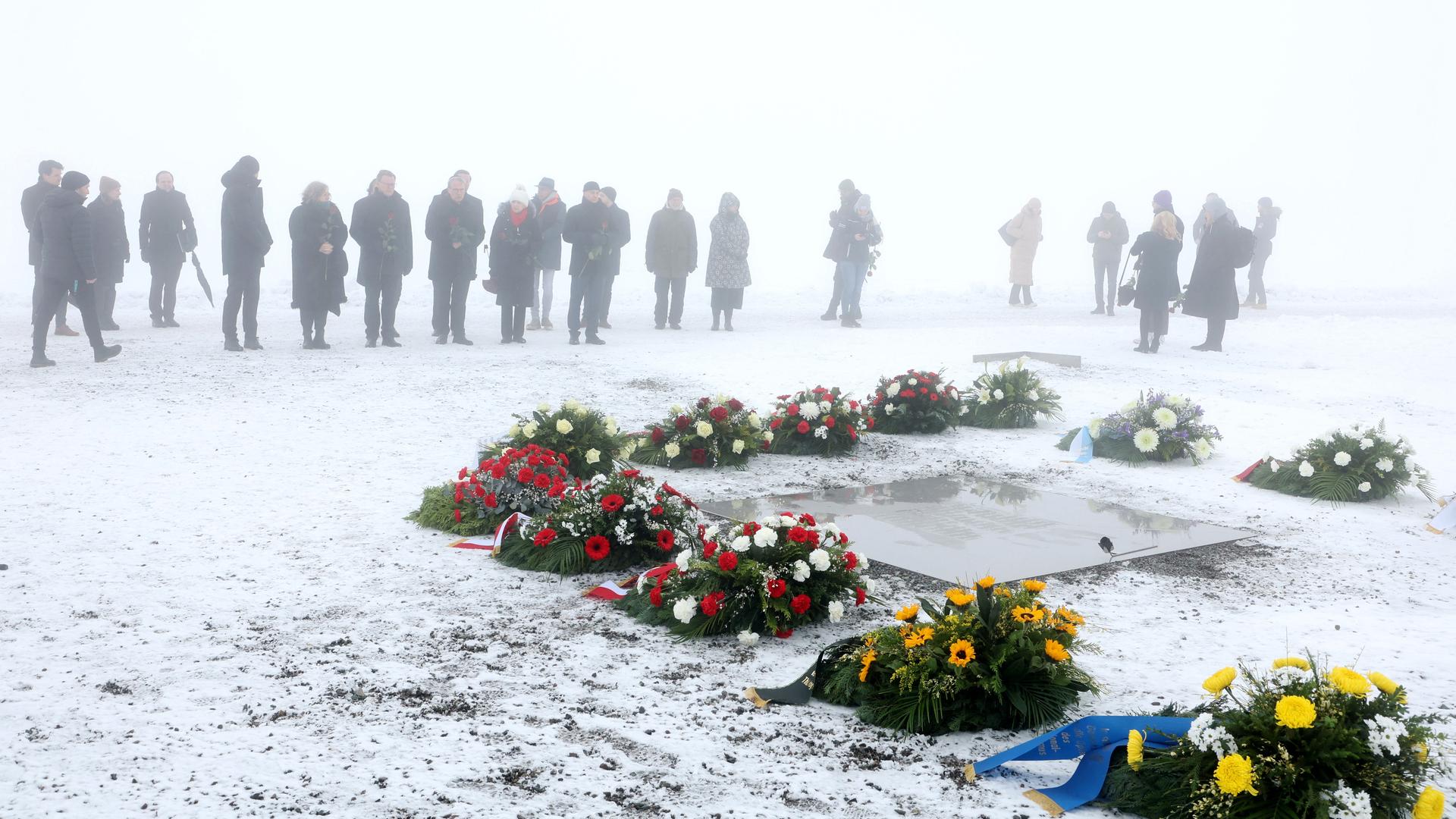 Teilnehmer stehen im Nebel bei einer Kranzniederlegung im ehemaligen Konzentrationslager Buchenwald vor Kränzen an einer Gedenkplatte. Der international begangene Holocaust-Gedenktag am 27. Januar erinnert an die Befreiung des deutschen Vernichtungslagers Auschwitz 1945.