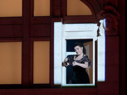 Cecilia Bartoli steht an einem beleuchteten Fenster und spielt Kastanietten.
