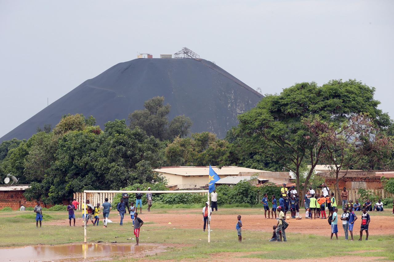 Ein belebter Fußballplatz mit spielenden Kindern in Lubumbashi, Kongo. Im Hintergrund ist eine große Mine zu sehen. Lubumbashi ist die Bergbauhauptstadt der Demokratischen Republik Kongo und fungiert als Drehscheibe für viele der größten Bergbauunternehmen des Landes. Ein belebter Fußballplatz mit spielenden Kindern in Lubumbashi, Kongo. Im Hintergrund ist eine große Mine zu sehen. Lubumbashi ist die Bergbauhauptstadt der Demokratischen Republik Kongo und fungiert als Drehscheibe für viele der größten Bergbauunternehmen des Landes.