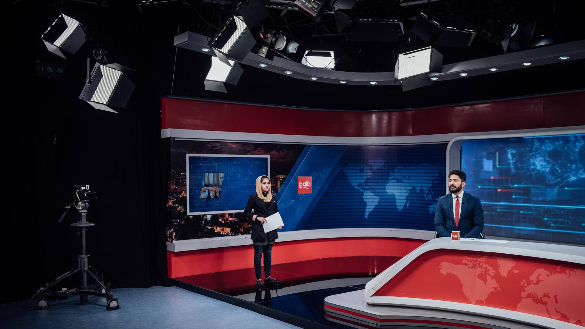 In einem Fernsehstudio steht eine Moderatorin, ein Moderator sitzt an einem Tisch. Sie blicken in unterschiedliche Kameras. In einem Fernsehstudio steht eine Moderatorin, ein Moderator sitzt an einem Tisch. Sie blicken in unterschiedliche Kameras.
