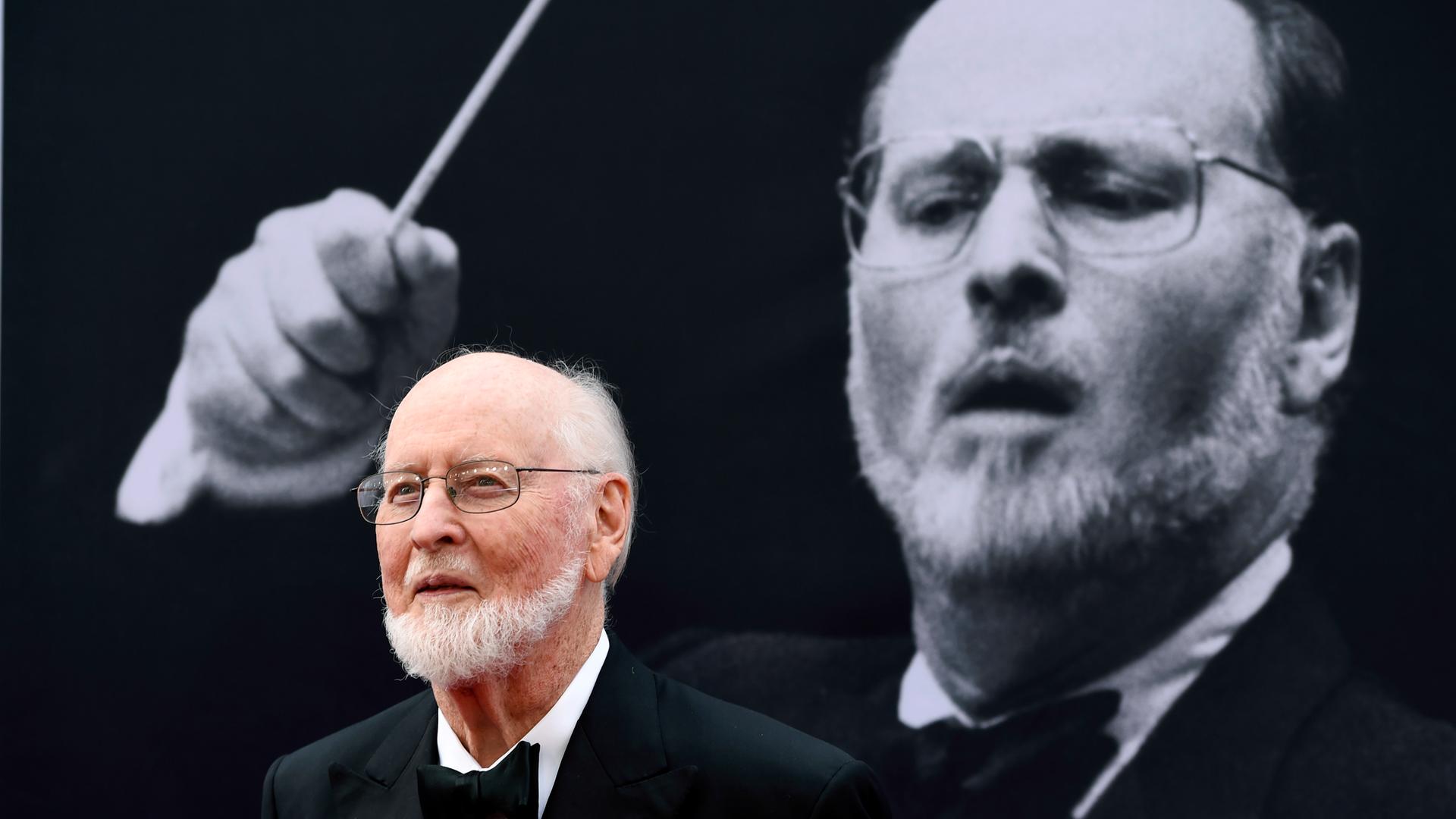 Der Dirigent und Filmkomponist John Williams mit einem Foto von ihm im Hintergrund. Der Dirigent und Filmkomponist John Williams mit einem Foto von ihm im Hintergrund.