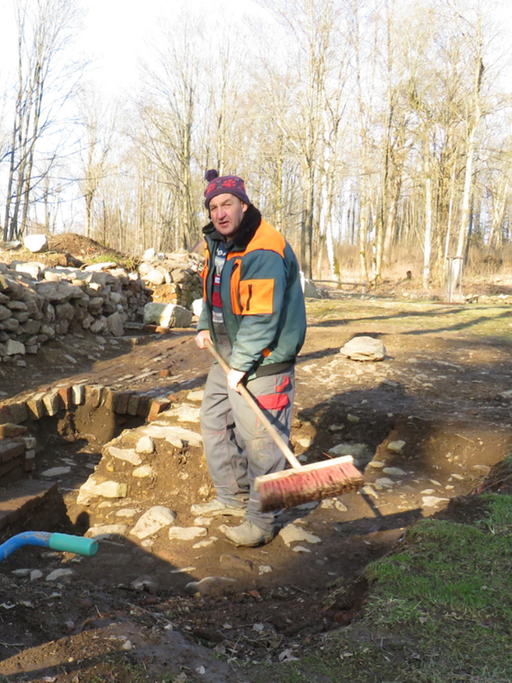 Helmut Roith fegt an der Grabungsstelle mit einem Besen die Mauerreste von Erde frei