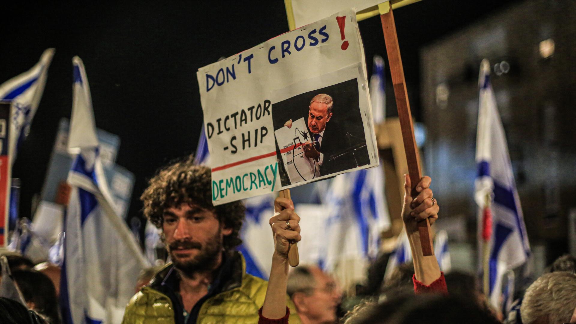Ein Demonstrant beim Protest gegen die israelische Regierung in Jerusalem hält ein Schild hoch mit einem Bild von Präsident Benjamin Netanjahu und dem Satz: "Don't cross! Dicatorship - Democracy".