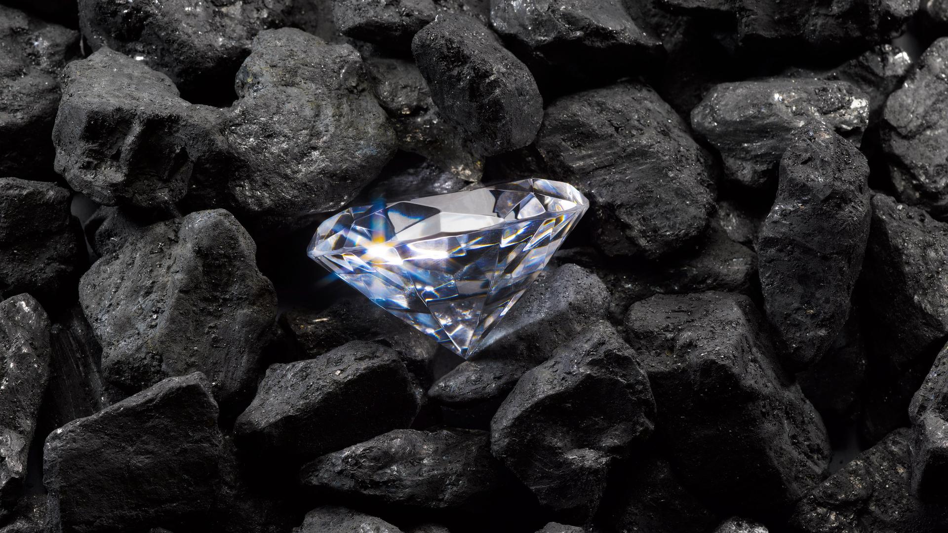 Ein funkelnder Diamant liegt auf einem Haufen schwarzer Steinkohle.