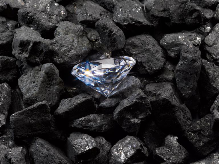 Ein funkelnder Diamant liegt auf einem Haufen schwarzer Steinkohle.