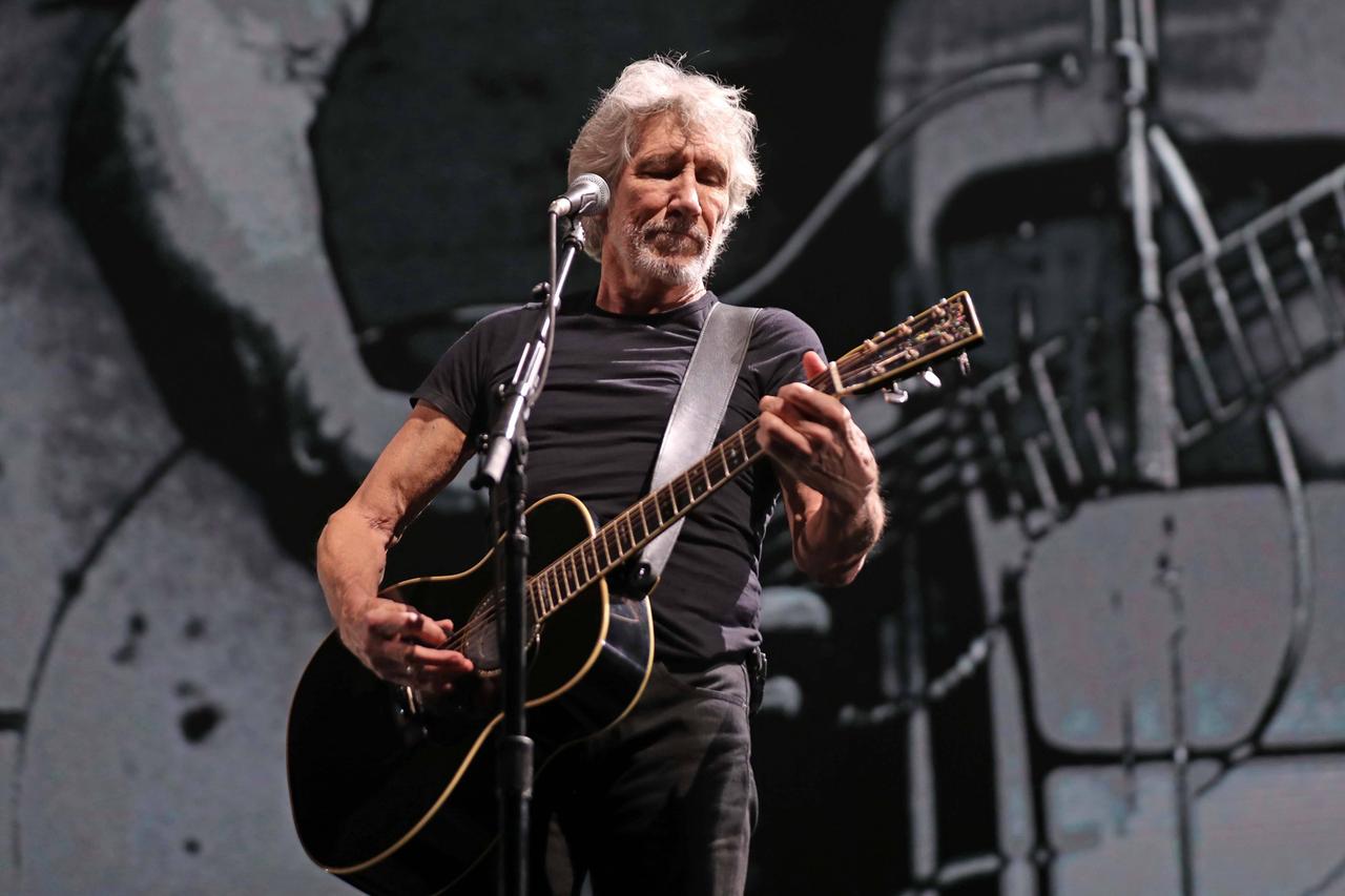 Der Pink Floyd-Mitgründer Roger Waters 2020 bei einem Konzert in Mexiko: Er steht auf einer abgedunkelten Bühne hinter einem Mikrofon und spielt eine akustische Gitarre.