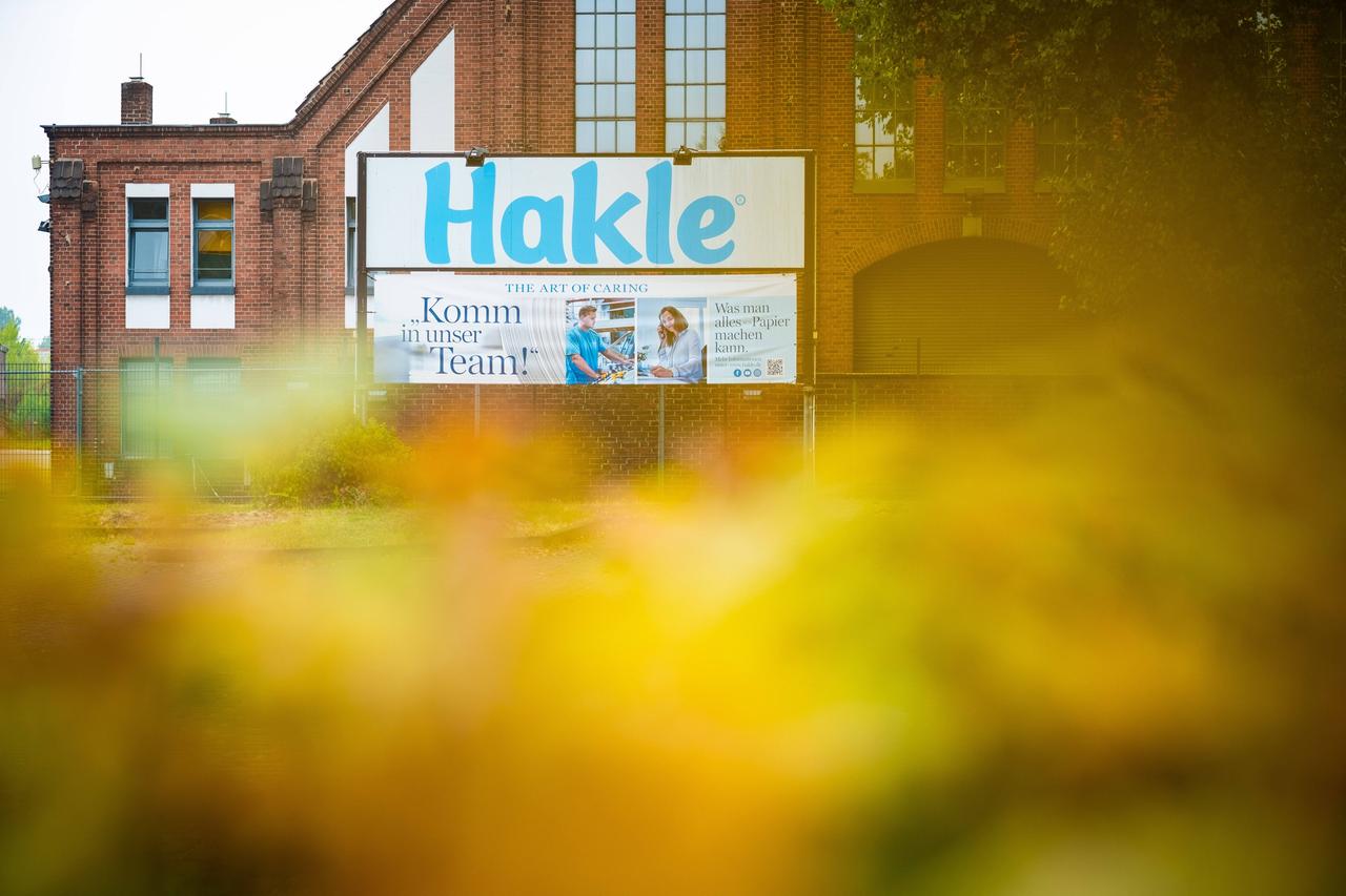 Vor einem roten Backsteingebäude steht ein Schild des Toilettenpapierherstellers Hakle mit der Aufschrift: „Komm in unser Team!"