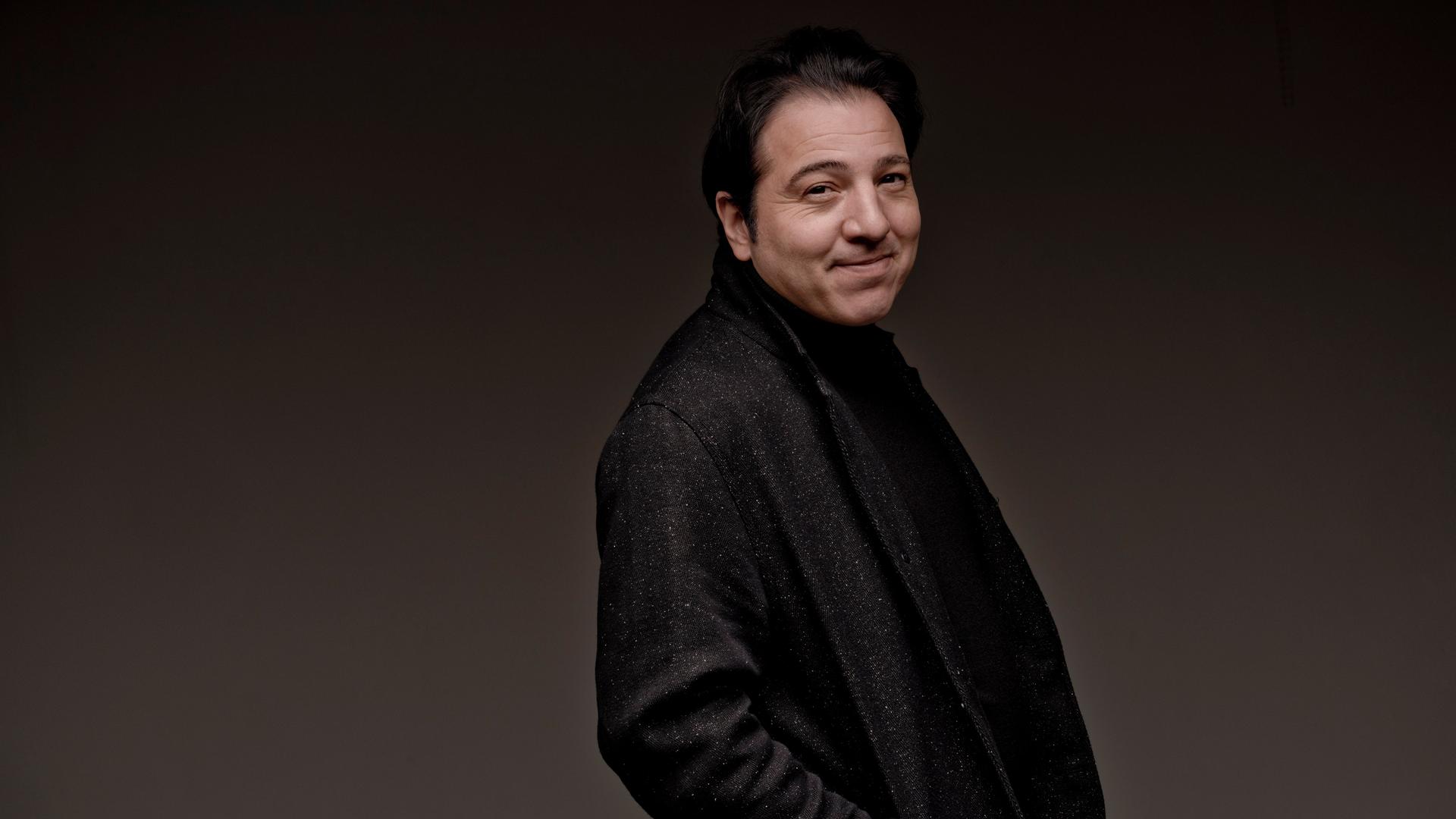 Ein Mann in einem dunklen Anzug steht und wendet den Kopf zur Kamera. Er blickt freundlich. Es ist der Pianist Fazıl Say. Ein Mann in einem dunklen Anzug steht und wendet den Kopf zur Kamera. Er blickt freundlich. Es ist der Pianist Fazıl Say.