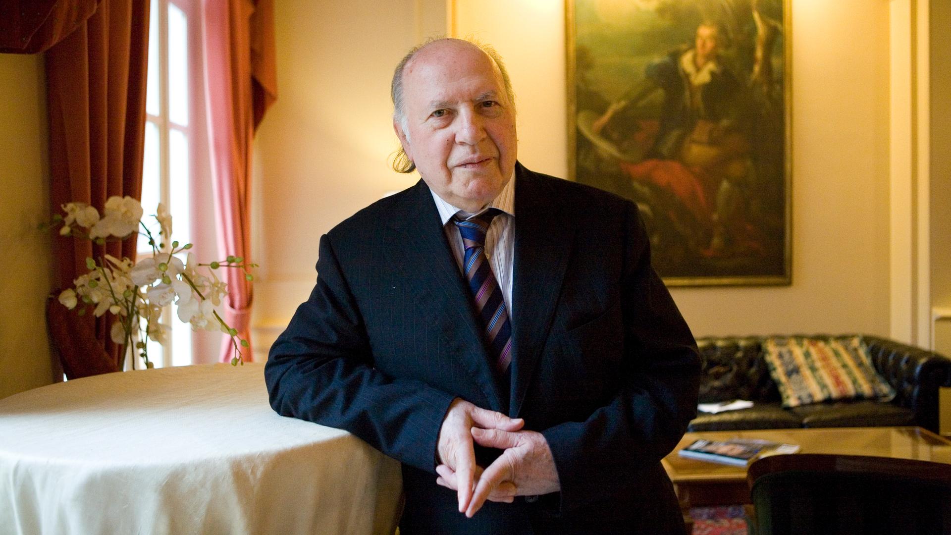 Imre Kertész lehnt sich in einem festlichen Raum an einen Stehtisch und blickt in die Kamera Imre Kertész lehnt sich in einem festlichen Raum an einen Stehtisch und blickt in die Kamera
