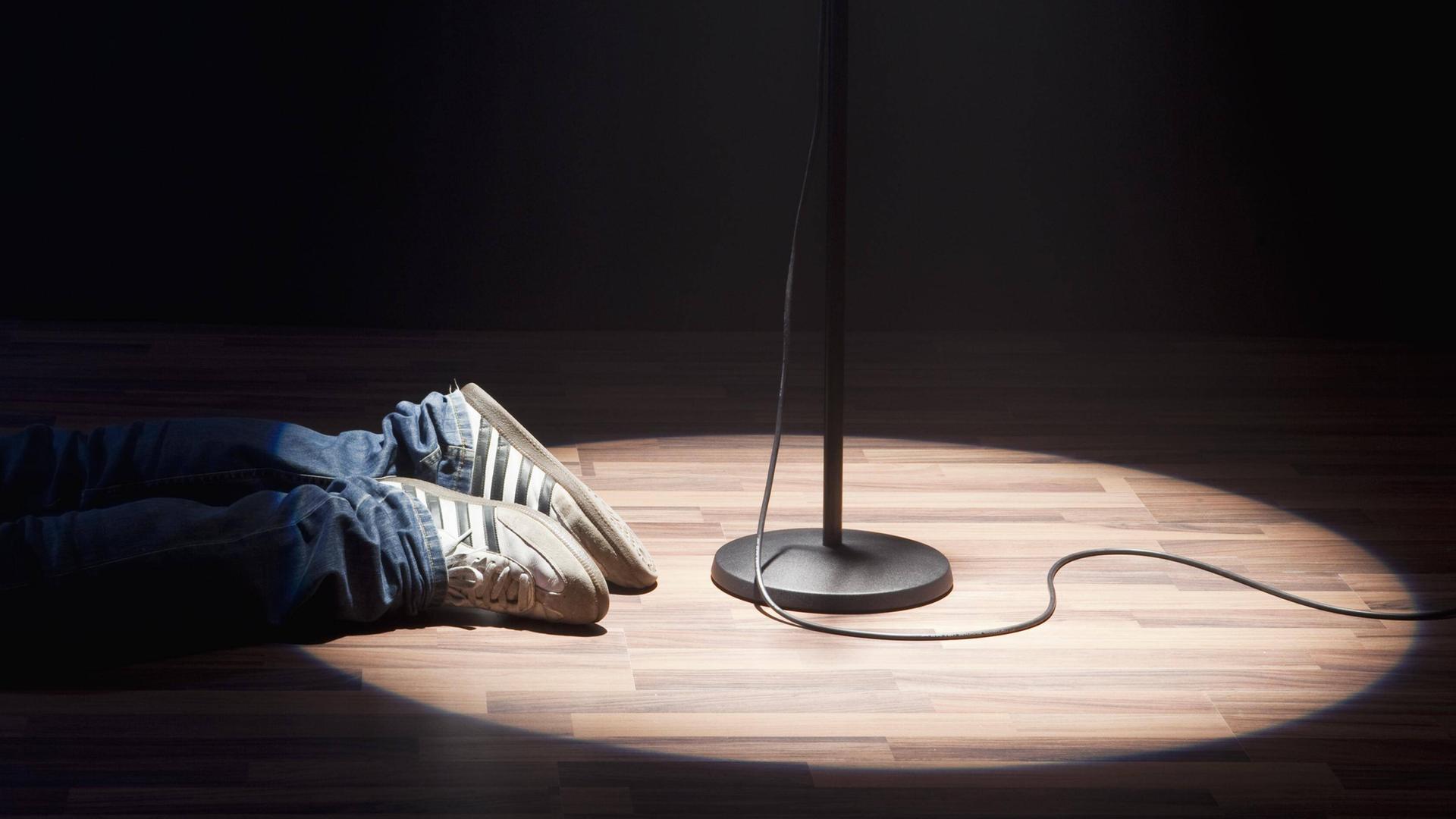 Eine Person liegt neben dem Spotlight eines Mikrofons, nur die Schuhe sind zu sehen. Eine Person liegt neben dem Spotlight eines Mikrofons, nur die Schuhe sind zu sehen.