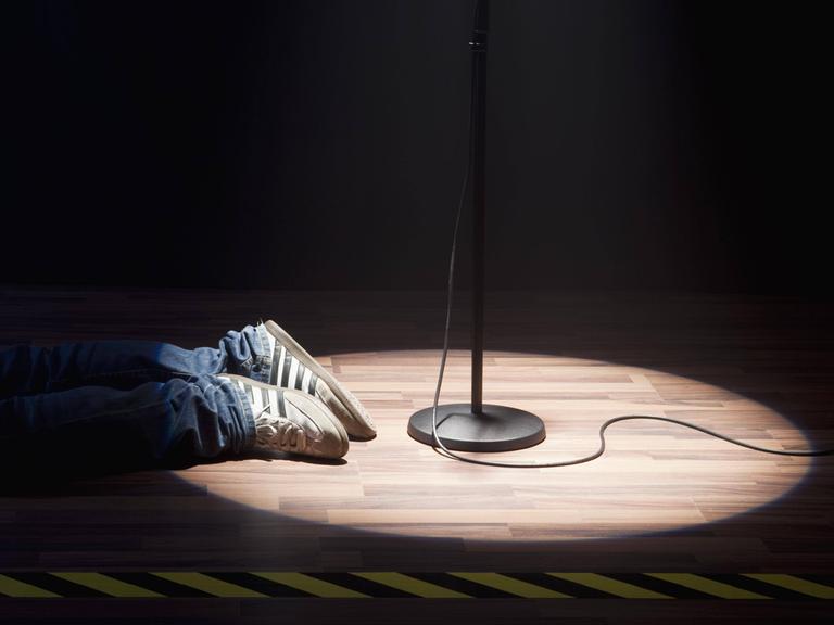 Eine Person liegt neben dem Spotlight eines Mikrofons, nur die Schuhe sind zu sehen.