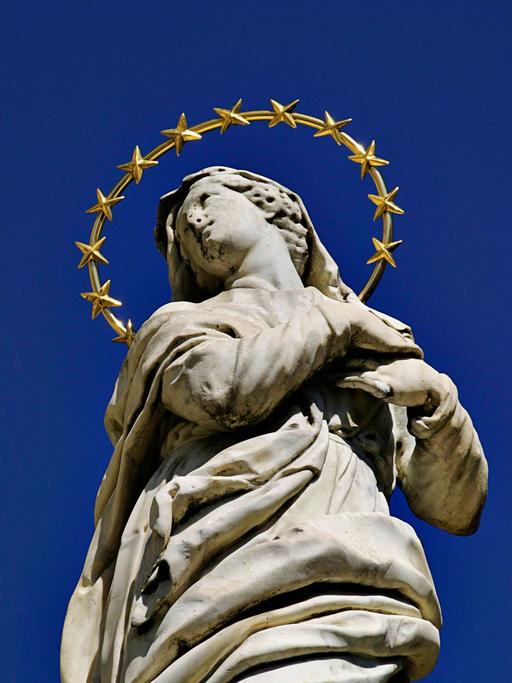 Die Marienstatue in Meran auf dem Sandplatz in Italien zeigt eine junge Frau in Stein mit aufgewühltem Gewand und einem großen Heiligenschein, der mit vielen Sternen geschmückt ist.