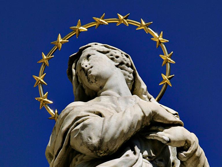Die Marienstatue in Meran auf dem Sandplatz in Italien zeigt eine junge Frau in Stein mit aufgewühltem Gewand und einem großen Heiligenschein, der mit vielen Sternen geschmückt ist.