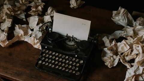 Eine Schreibmaschine mit einem leeren Blatt Papier, umgeben von zerknülltem Papier. 