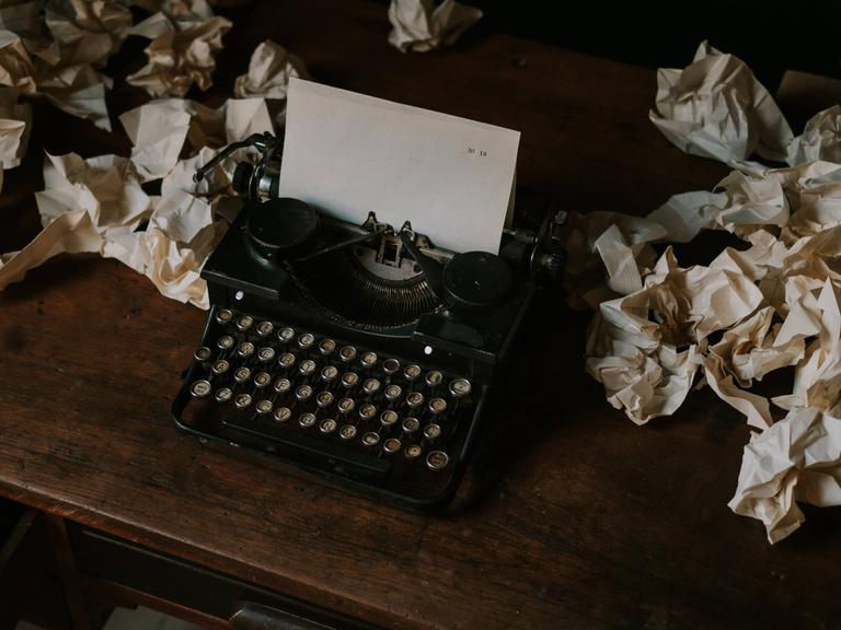 Eine Schreibmaschine mit einem leeren Blatt Papier, umgeben von zerknülltem Papier. 