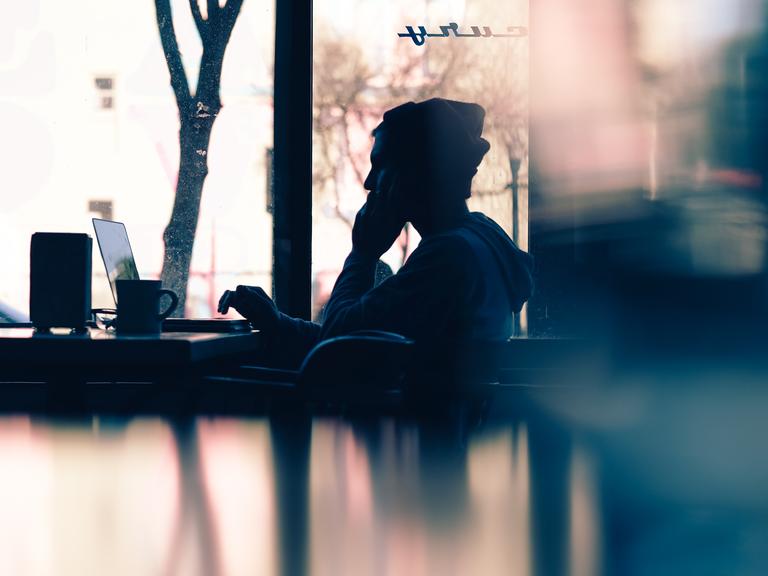 Ein Mann arbeitet am Laptop und telefoniert dabei