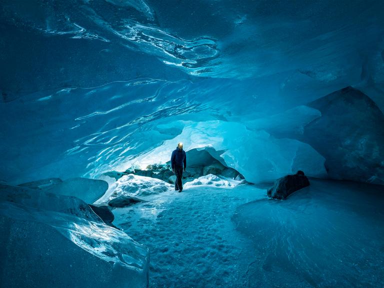 Mann mit Stirnlampe geht in die Gletscherhöhle des Morteratsch-Gletschers in der Schweiz.